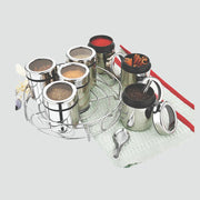 Stainless steel spice jars with transparent lids in a rotating rack on a kitchen mat with cinnamon sticks and peppercorns